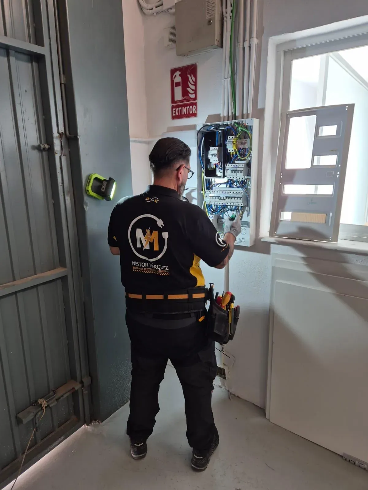 Néstor Márquez trabajando en un cuadro eléctrico, de espaldas y con el uniforme de la empresa